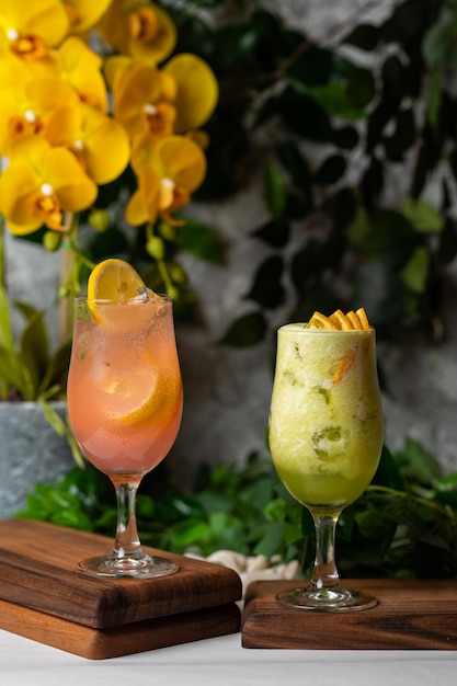 Two cocktails on a bar with yellow orchids in the background