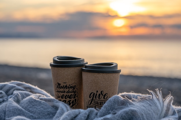 Две чашки кофе в одеяле на пляже на закате