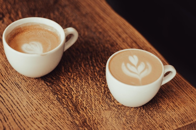 Two coffee cups on wooden table Latte art concept Coffee with milk in white cup Breakfast table