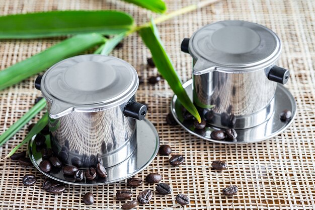 Two coffee makers with scattered whole coffee beans on placemat.