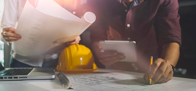 Two colleagues discussing data working and tablet laptop with\
on on architectural project at construction site at desk in\
office