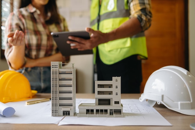 Two colleagues discussing data working and tablet laptop with on on architectural project at construction site at desk in officexA