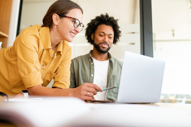 two colleagues have pleasant conversation sitting side by side in modern open space office smiling and enjoying friendly working atmosphere