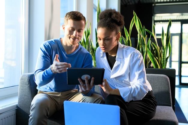 Two colleagues look at the tablet screen and discuss a new project in the office