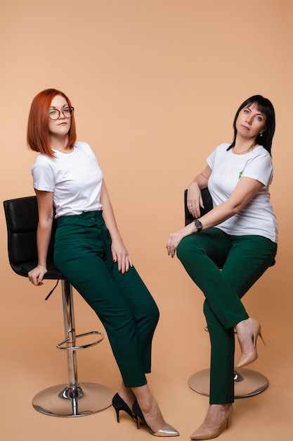 Two colleagues sitting on bar stools. Two pretty young adult women in corporate look posing on bar stools.