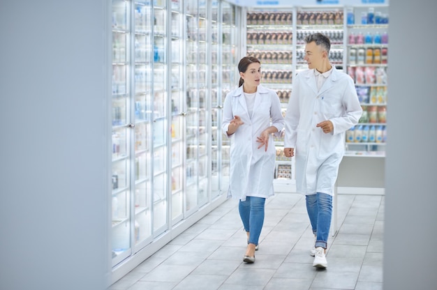 Two colleagues in white coats walking around pharmacy