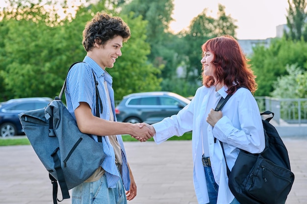 two college classmates guy and girl with backpacks met outdoors greeting handshake