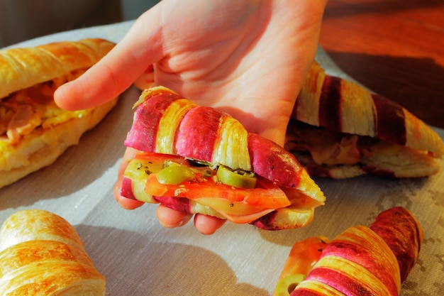Foto croissant a due colori riempito di semi-pizza, prosciutto, formaggio e pomodoro tenuto dalla mano di una donna