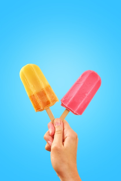 Two color popsicles in woman hands on blue background