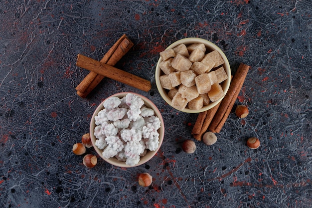 Two colorful bowls full of sweet white and brown candies with healthy nuts and cinnamon sticks 