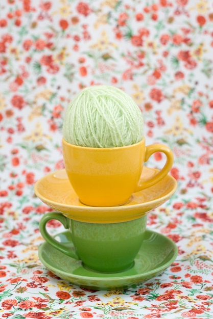 Two colorful cups and balls of yarn on a background of a red flower