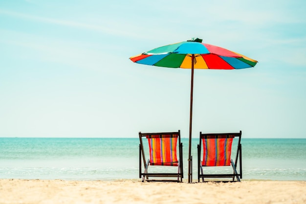Foto due sedie a sdraio colorate e un ombrello colorato vacanze estive in spiaggia sabbiosa tropicale e concetti di vacanze estive