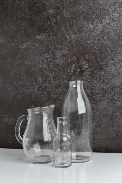 写真 形と大きさの異なる無色透明のガラスびん 2 本と、暗い場所に置かれたガラス ピッチャー