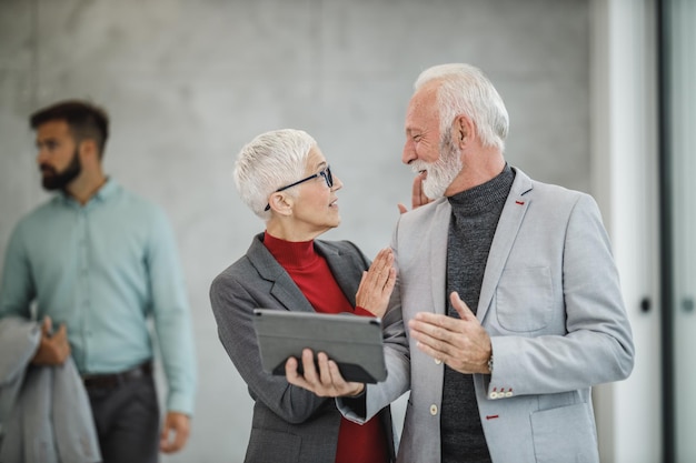 A two confident senior business people using a digital tablet in a modern office.