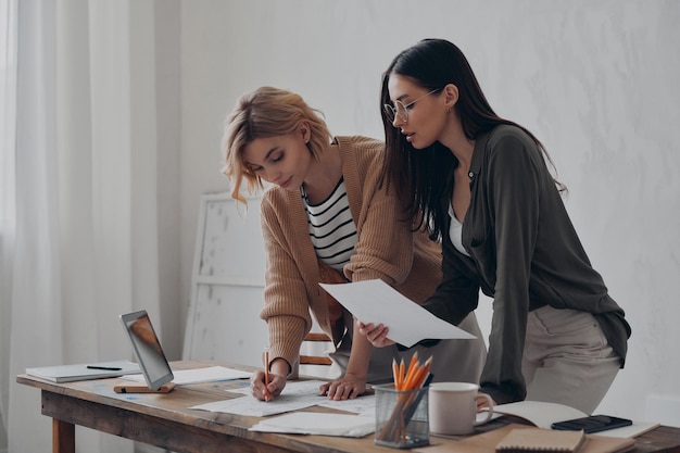 two confident young female colleagues working with papers in the office together