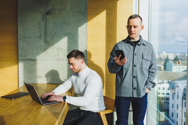 Photo two confident young people are sitting together at a table and one of them is pointing at a laptop work on a new project successful colleagues working together in the office