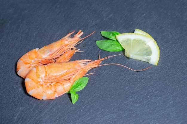 Two cooked red prawns with green basil and lemon on black backgeound