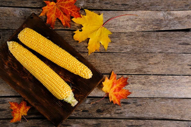 Photo two corn on wooden chopping board and autumn maple leaves falling on table