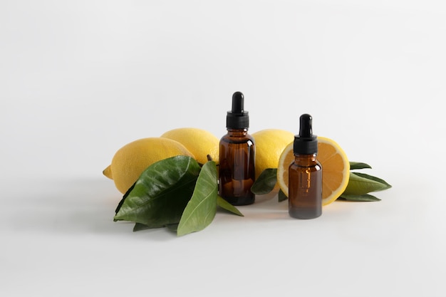 Фото Две косметические бутылки с пипеткой с сывороткой на основе эфирного масла лимона на белом фоне со спелыми фруктами, омолаживающим эффектом витамина с