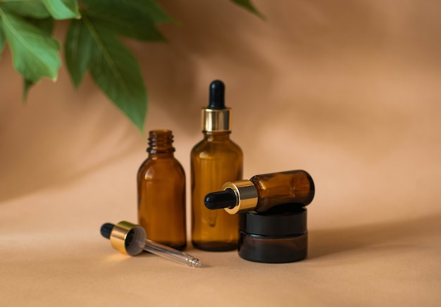 Two cosmetic bottles with a pipette stand and one lies on a cosmetic jar on a beige background