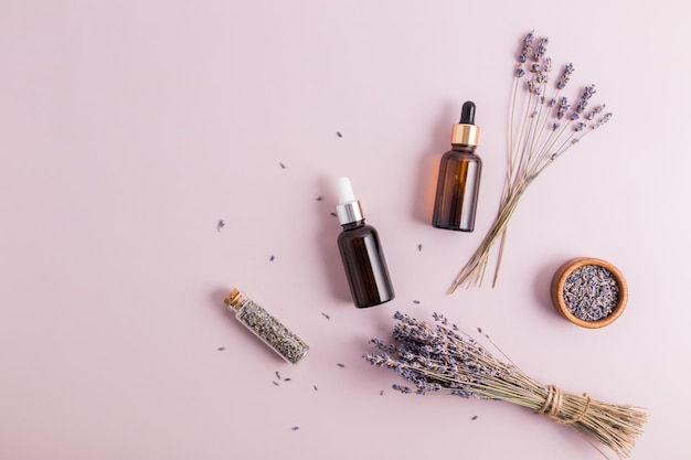 Two cosmetic bottles with a pipette with natural serum or lavender on a purple background with a bouquet and flower seeds top viewcopy of the space