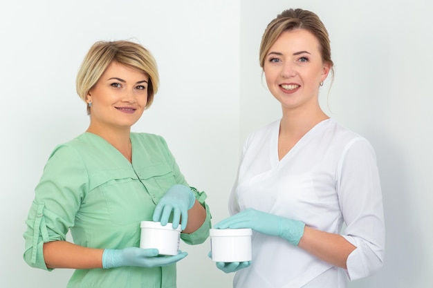Two cosmeticians with jars of wax for depilation smiling against a white background. Natural product for hair removal. Copy space.