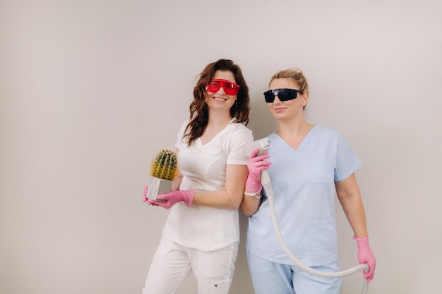 Два косметолога в защитных очках держат в руках устройство для лазерной депиляции и кактус