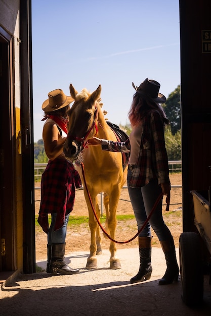 Two cowgirl women entering the stable with a horse on a horse with South American outfits