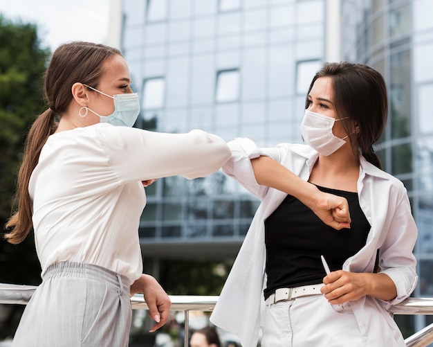 Photo two coworkers touching elbows outdoors during pandemic while wearing masks