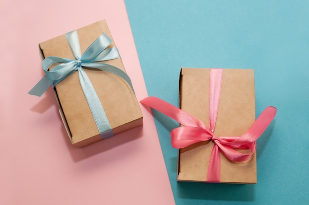 Two craft gift boxes tied with pink and blue satin ribbons on pink and blue backgrounds