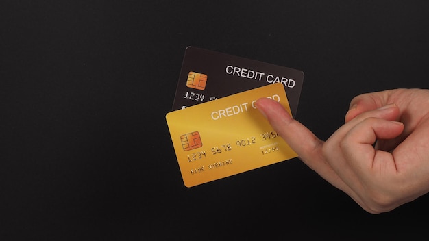 Due carte di credito in colore nero e oro in mano su sfondo nero.