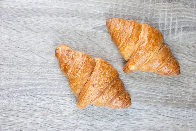 Two croissant are placed on a gray wooden table