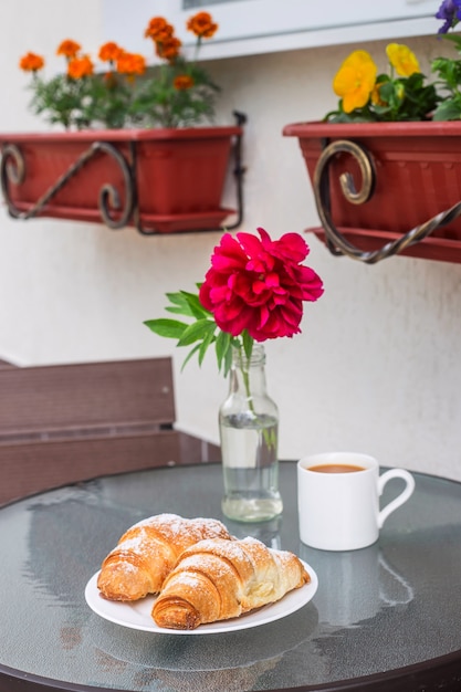 Two croissants on a plate next to a cup of cappuccino on a street table 