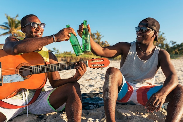 Photo two cuban friends having fun in the beach with his guitar. friendship concept.