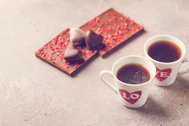 Two Cup of coffee with love and chocolate candies in a heart shape over gray background for Valentine's day conception