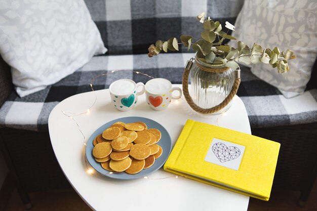 두 잔의 커피와 맛있는 팬케이크가 테이블, 노란색 사진 앨범에 서 있습니다.