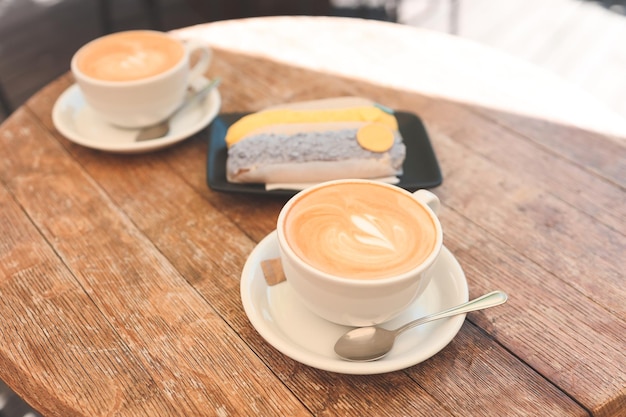 Two cups of coffee and an eclair on a wooden background