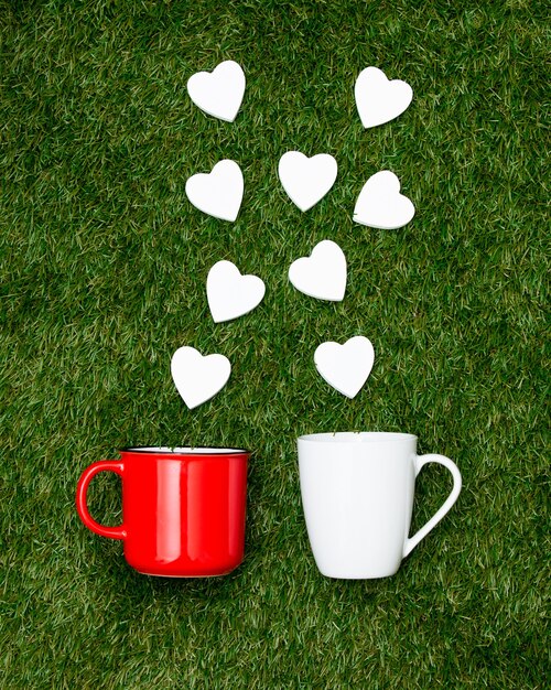 Two cups of coffee and heart shapes on green grass.