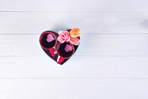 Two cups of coffee, macaroons, flowers in a box form of a heart on a white background.