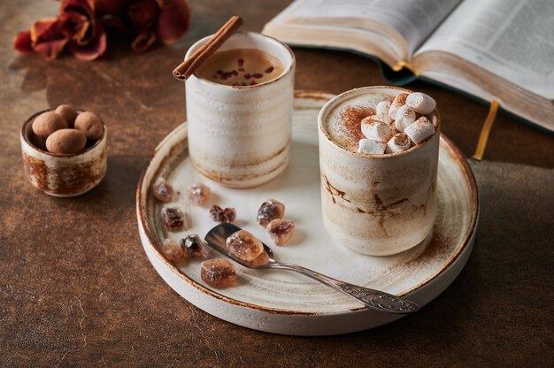 Two cups of coffee with foam and marshmallow and sublimated raspberries with cinnamon on light plate