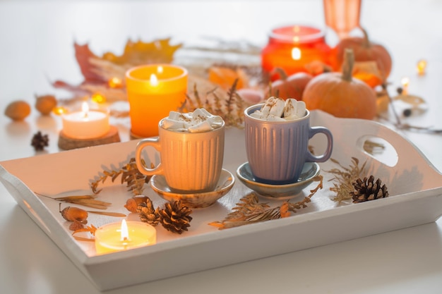 Two cups of  coffee  with marshmallows  and autumn decor on white wooden tray