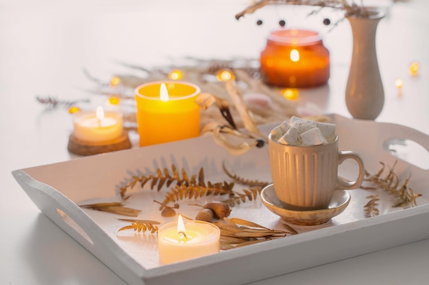 Two cups of coffee with marshmallows and autumn decor on white wooden tray