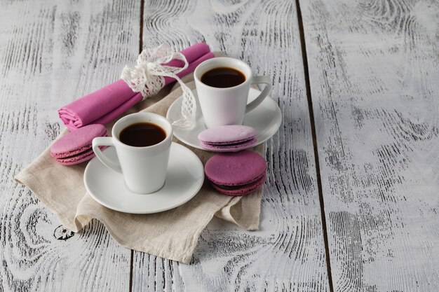 Two cups of espresso with macaroons on rustic table.