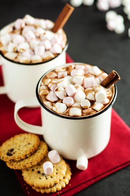 Two cups of hot chocolate, cocoa or warm drink with marshmallows and sweet cookies on dark 