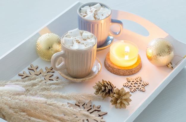 Two cups of  hot drink with marshmallows  and christmas decor on white wooden tray