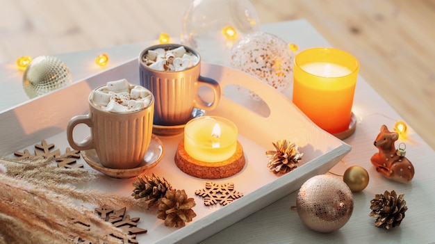 Two cups of  hot drink with marshmallows  and christmas decor on white wooden tray