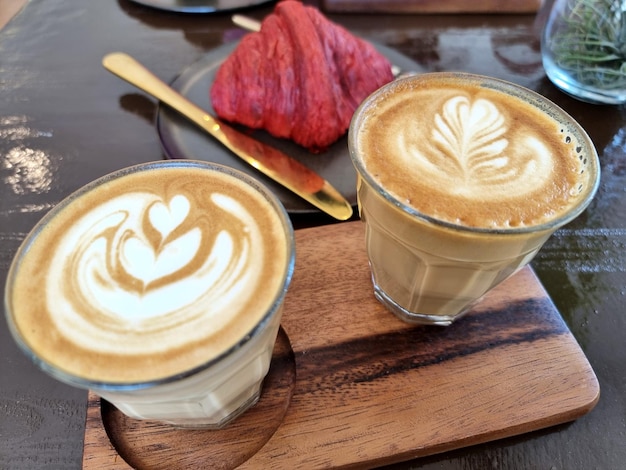 Two cups of hot latte art coffee with a red velvet croissant