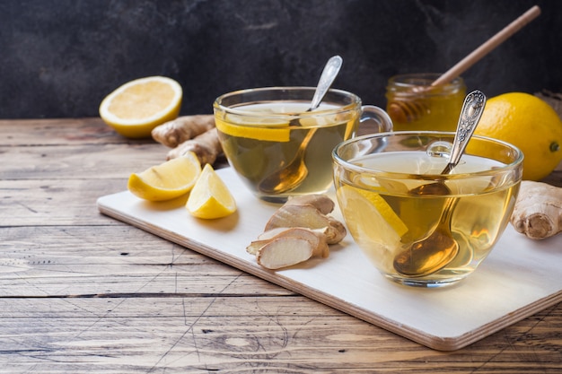 Two cups of natural herbal tea ginger lemon and honey on a wooden surface. 