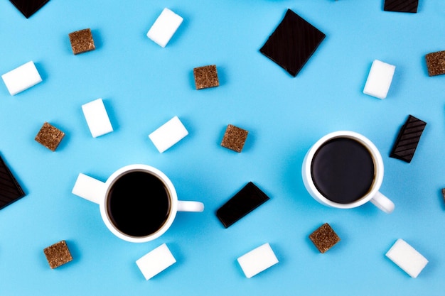 Фото Две чашки кофе коричневые и белые кубики сахара и шоколадные цены на синем фоне