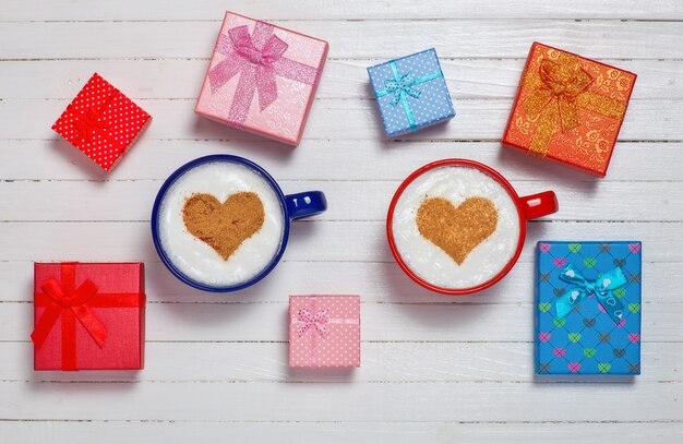 Фото Две чашки кофе с символом в форме сердца и подарочные коробки на деревянном белом фоне